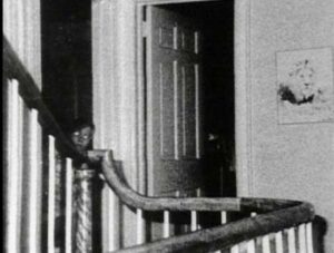 The picture. which appears to be of a small boy with glasses or a man kneeling on the floor with glowing eyes, has been called everything from one of the dead DeFeo children to a demon, first turned up in the collection of photos George Lutz had from an investigation into the haunting in 1976, led by infamous Demonologists Ed and Lorraine Warren.